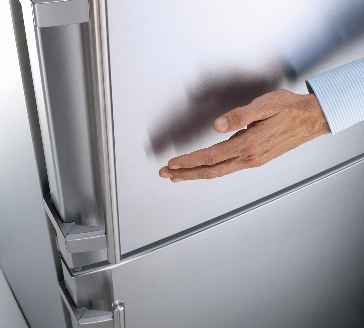 A hand is reaching towards a stainless steel refrigerator door, highlighting its sleek surface.