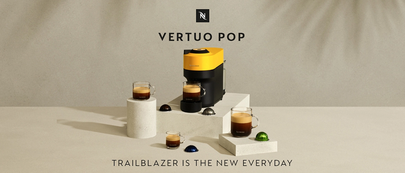 A coffee machine with a yellow top, surrounded by coffee cups and colorful capsules, set against a neutral background.